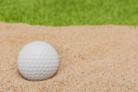 White golf ball in sand bunker on golf court.